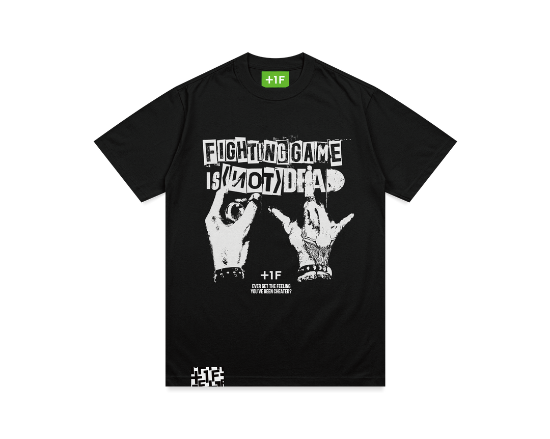 黒いTシャツの表面。胸元にプリントデザイン、「FIGHTING GAME IS (NOT) DEAD TEE」の文字とアーケードコントローラーを握る手がメタル風にデザイン。襟タグは明るい緑色で白い「+1F」のロゴ入り、前右裾にはピスネーム。